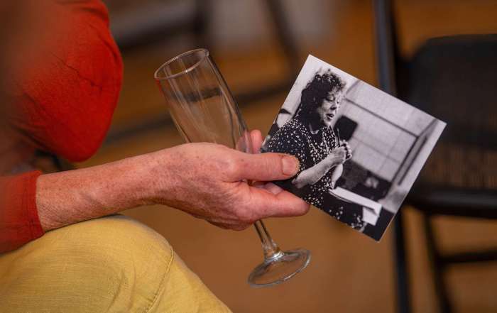 A hand holding a black and white photo of Annie Castledine along with an empty prosecco glass